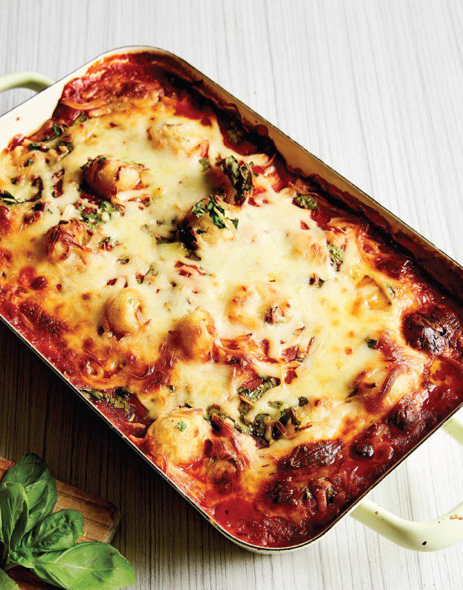 A family-sized baking tray of baked gnocchi with cheesy bubbles on top.