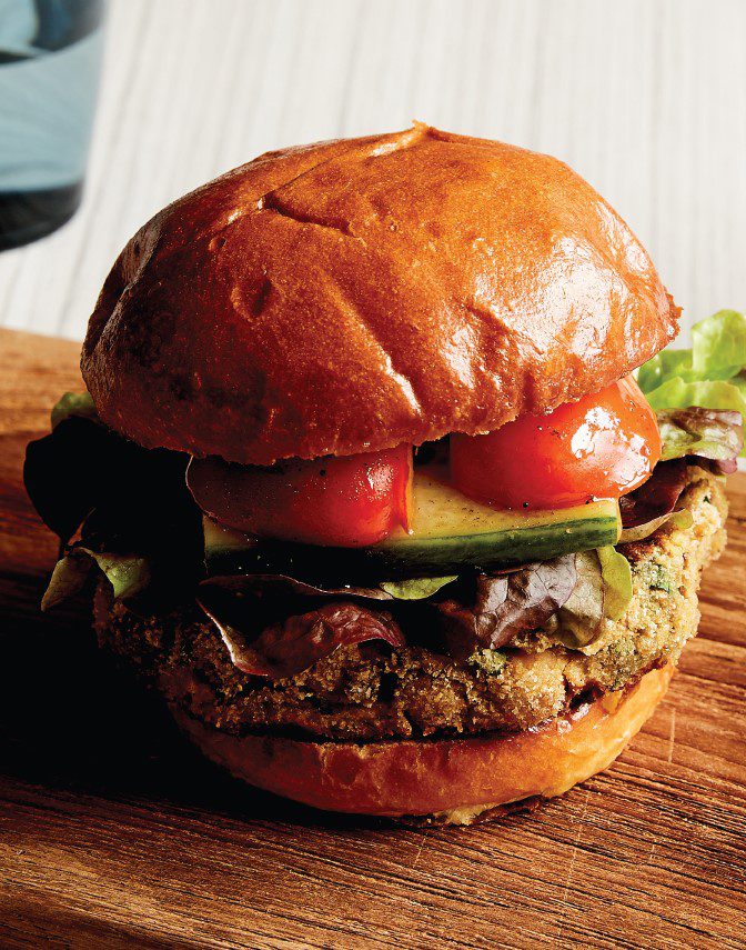 A close-up of a burger filled with colourful vegetables and lentil patty, in a brioche bun.