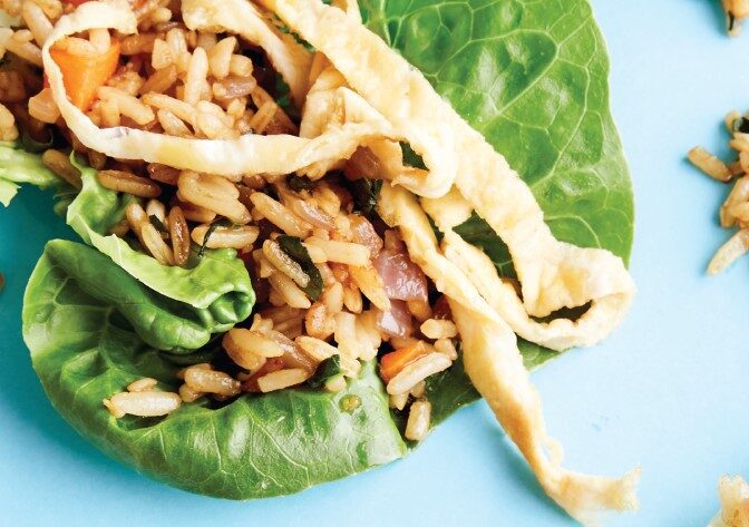 A close-up of crisp baby cos lettuce cups, filled with colourful fried rice and ribbons of egg on top.