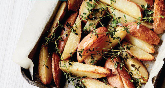 A rustic baking tray scatted with crispy wedges of potato, sprinkled with fresh thyme sprigs.